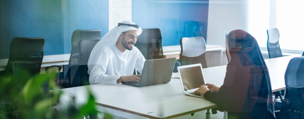 Man and woman with traditional clothes working in a business office of Dubai. Portraits of  successful entrepreneurs businessman and businesswoman in formal emirates outfits. Concept about middle eastern cultures, lifestyle and professional occupations